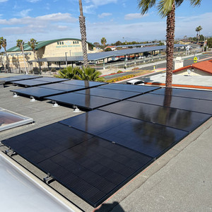 Black rooftop solar array on a flat roof with palm trees and blue sky