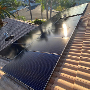 Solar panels spanning two tile roofs with palm trees behind